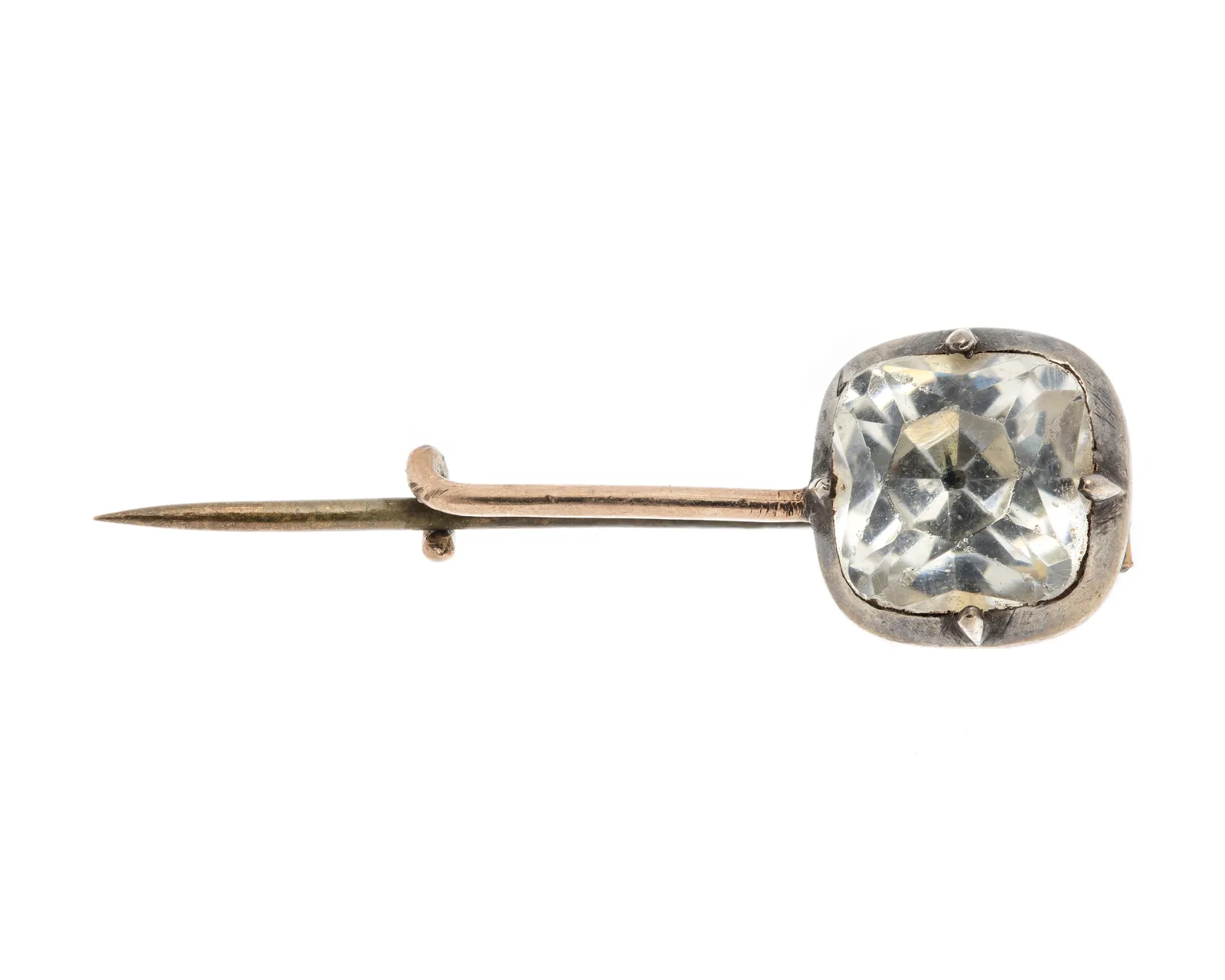 A gold brooch with an oval rock crystal at the center, surrounded by gold scrolls and small leaves, on a white ground
