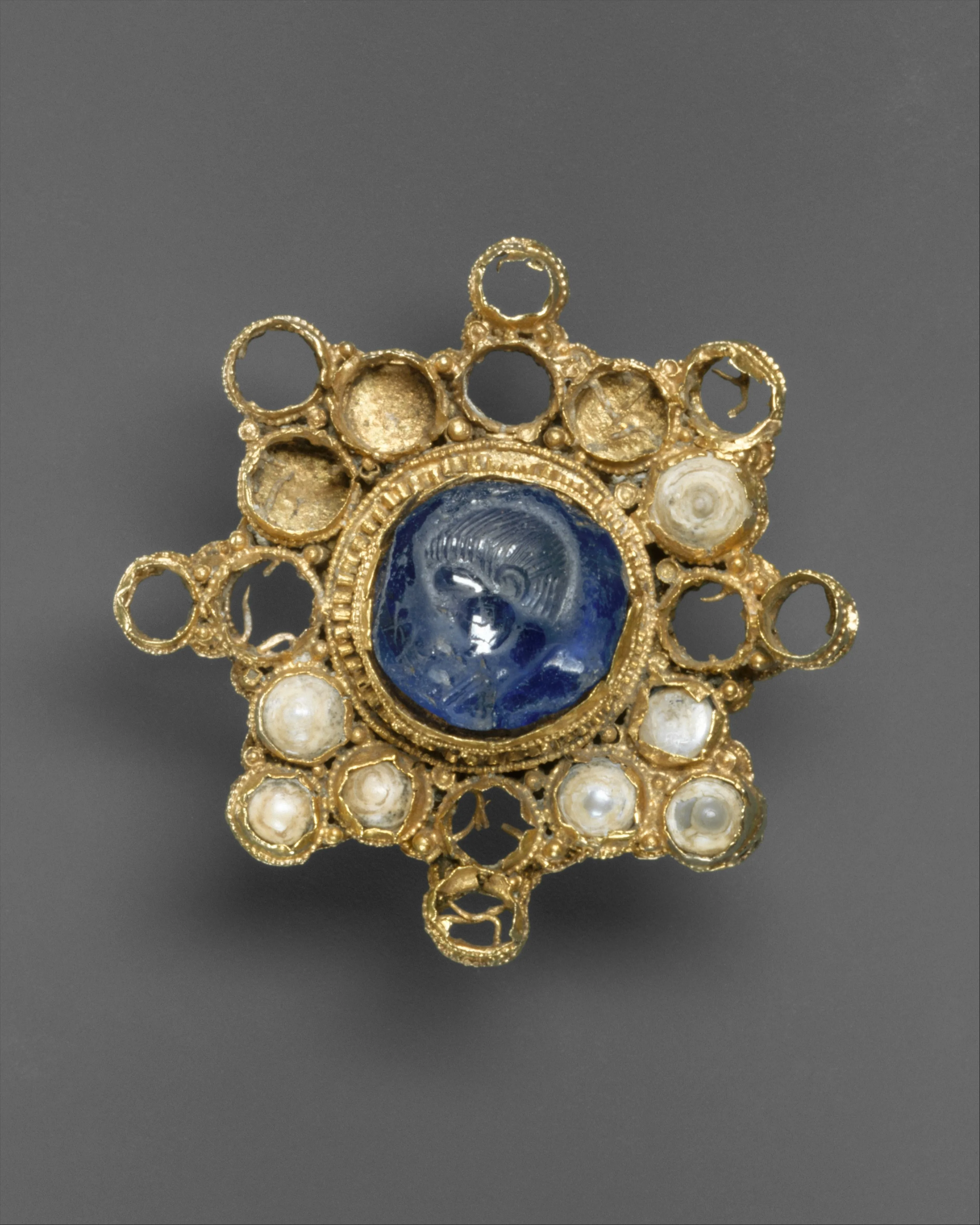Ottonian gold star brooch with a blue star-sapphire intaglio of an emperor at the center and a ring of pearls, gold loops as the points