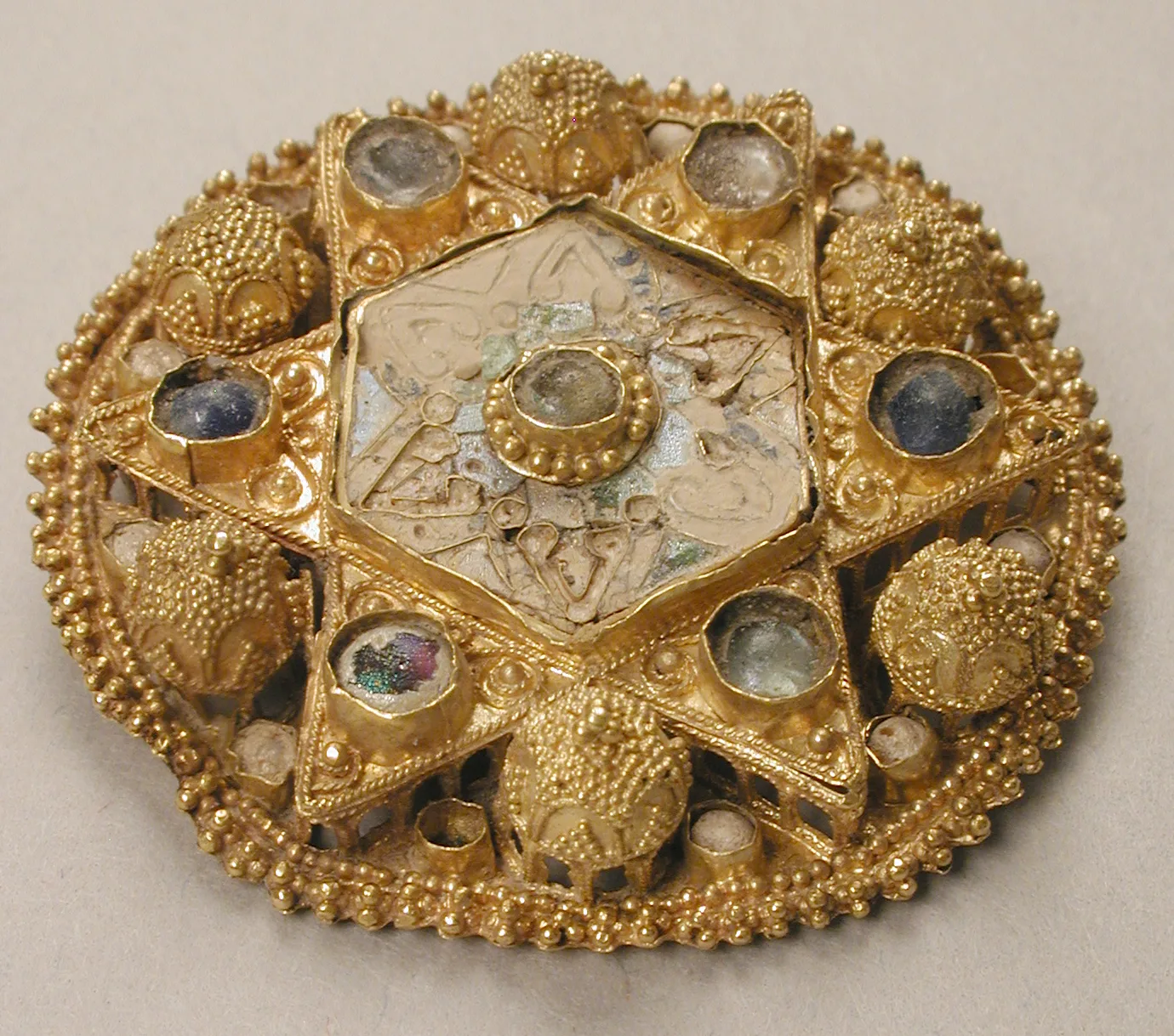 Ottonian gold star brooch with a hexagonal pale enamel center, glass and pearl settings, and six gold points