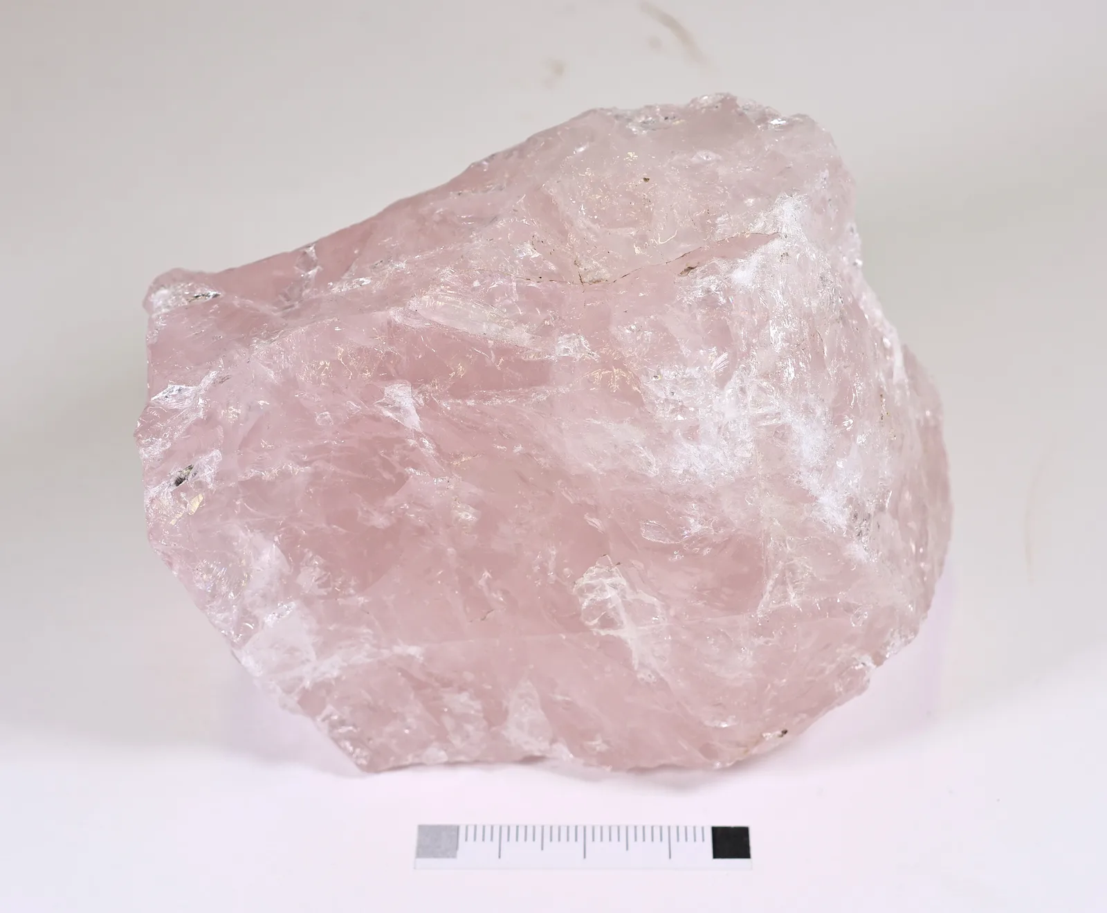 A rough piece of milky pink rose quartz from Madagascar, translucent at the edges, with a millimeter scale