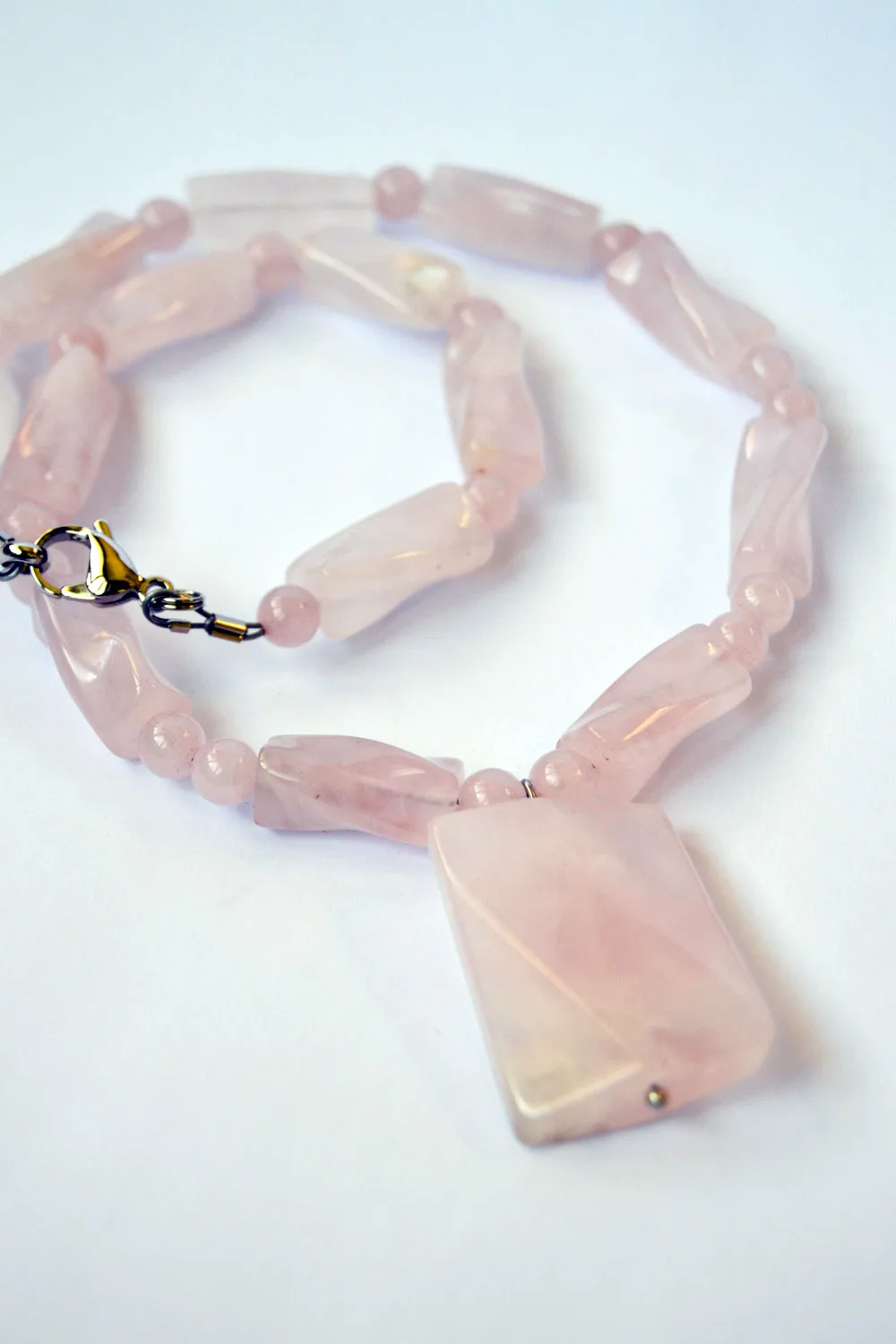 A strand of polished rose quartz beads in a soft milky pink, laid in a loose curve on a white ground