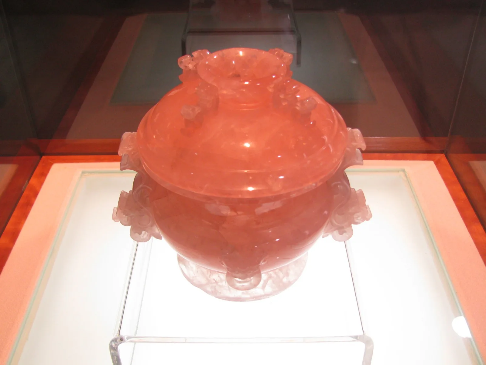 A carved rose quartz censer with a dragon head, pale translucent pink, on a museum stand