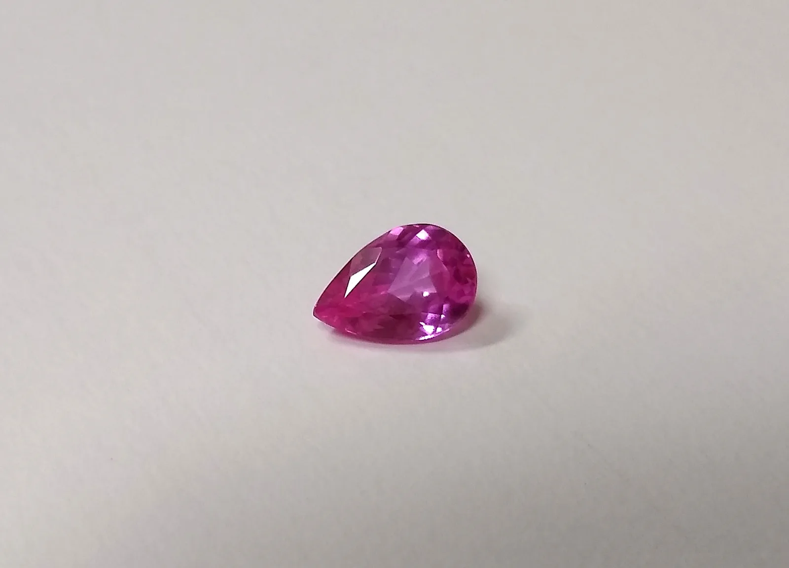 An oval faceted rubellite, saturated pink, on a white ground