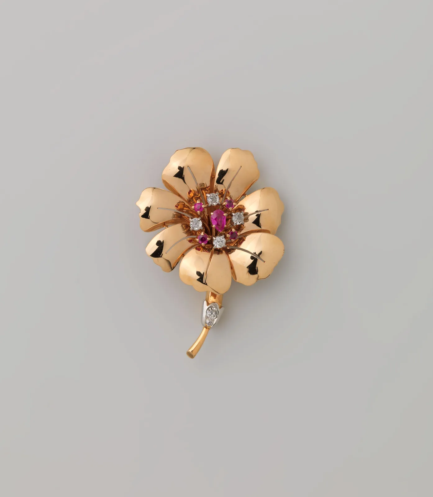 Gold flower brooch with a central ruby and diamonds, resting in an open box