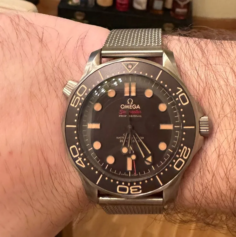 Omega Seamaster Diver 300M with a blue wave-engraved dial and a ceramic bezel, shown off the wrist on a pale ground