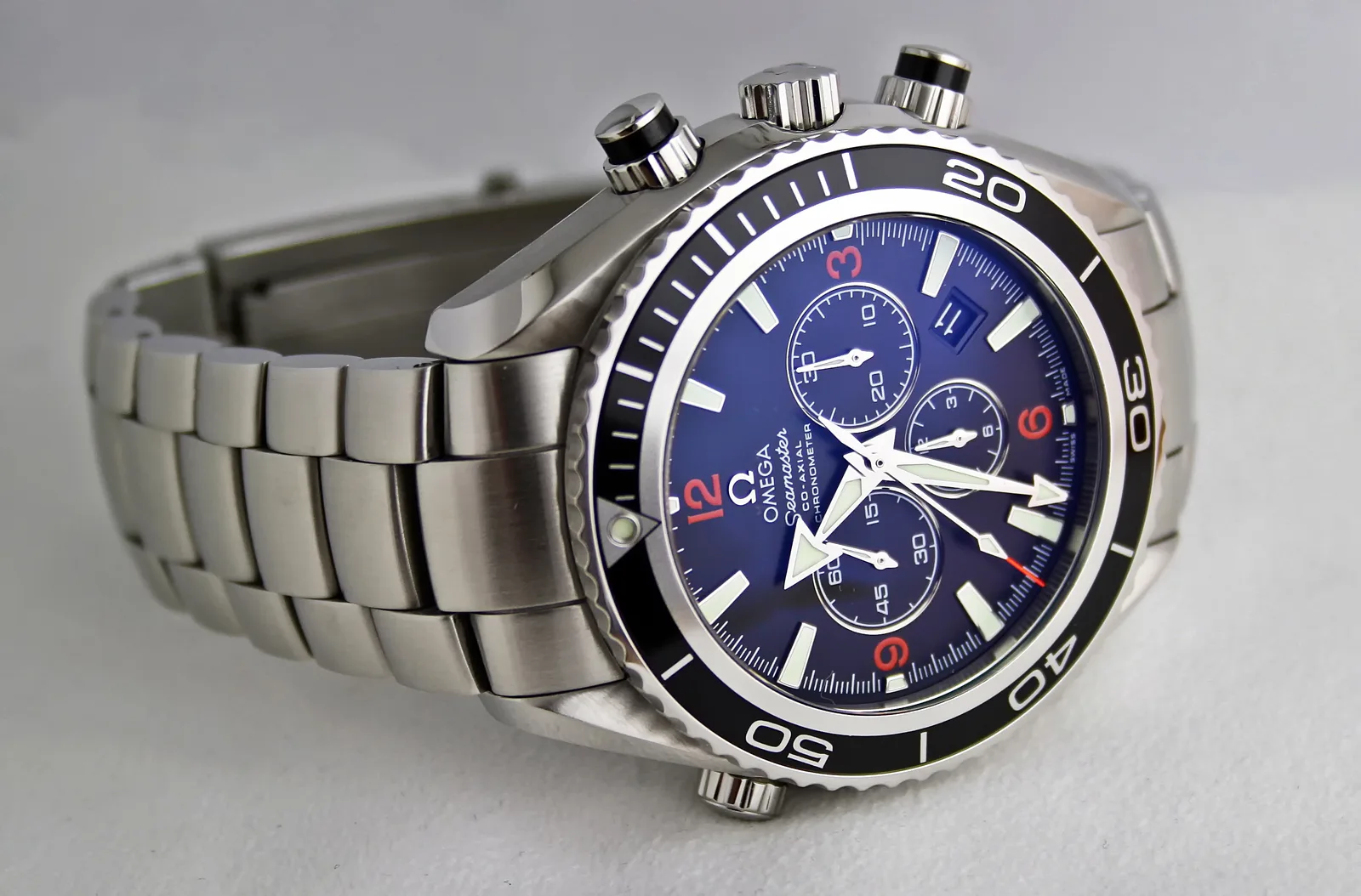 Omega Seamaster Planet Ocean Chronograph reference 2210.51.00 with an orange ceramic bezel, shown off the wrist on a pale ground