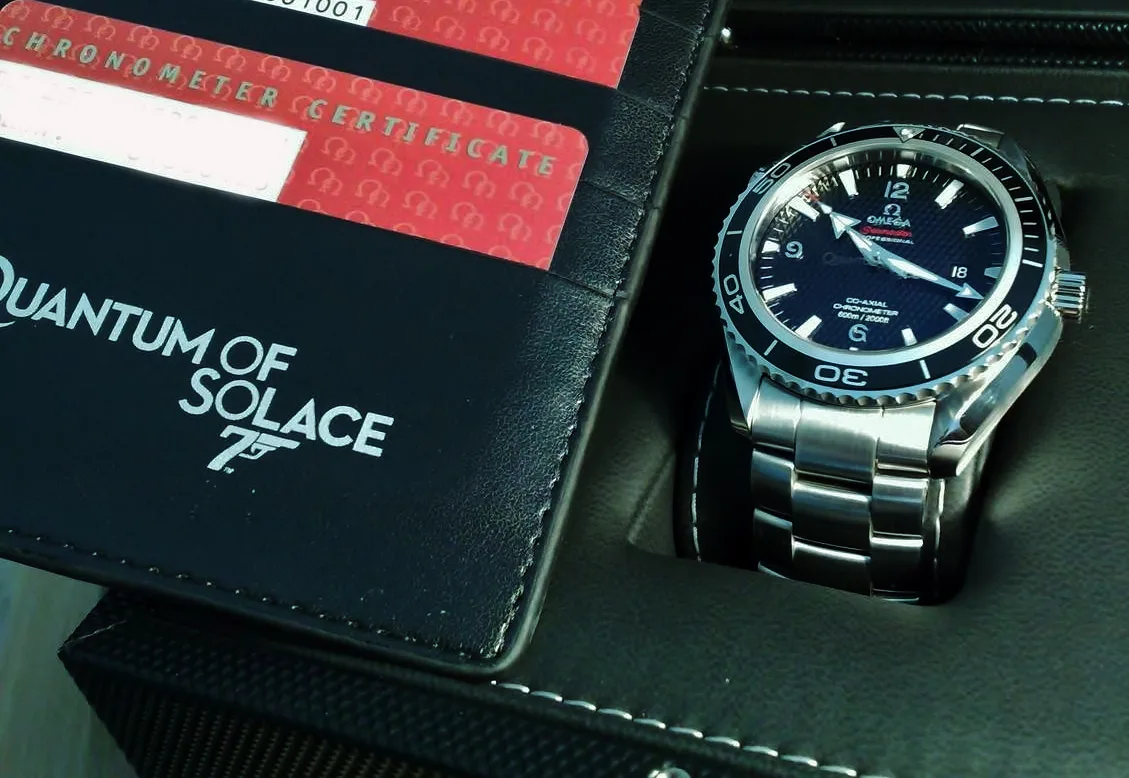 Omega Seamaster Planet Ocean with a black wave dial and a dark bezel, shown off the wrist on a white ground