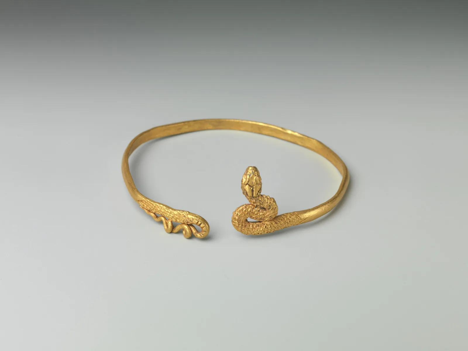 Ptolemaic gold child’s bracelet, a slim hoop ending in a raised snake head and a waving tail