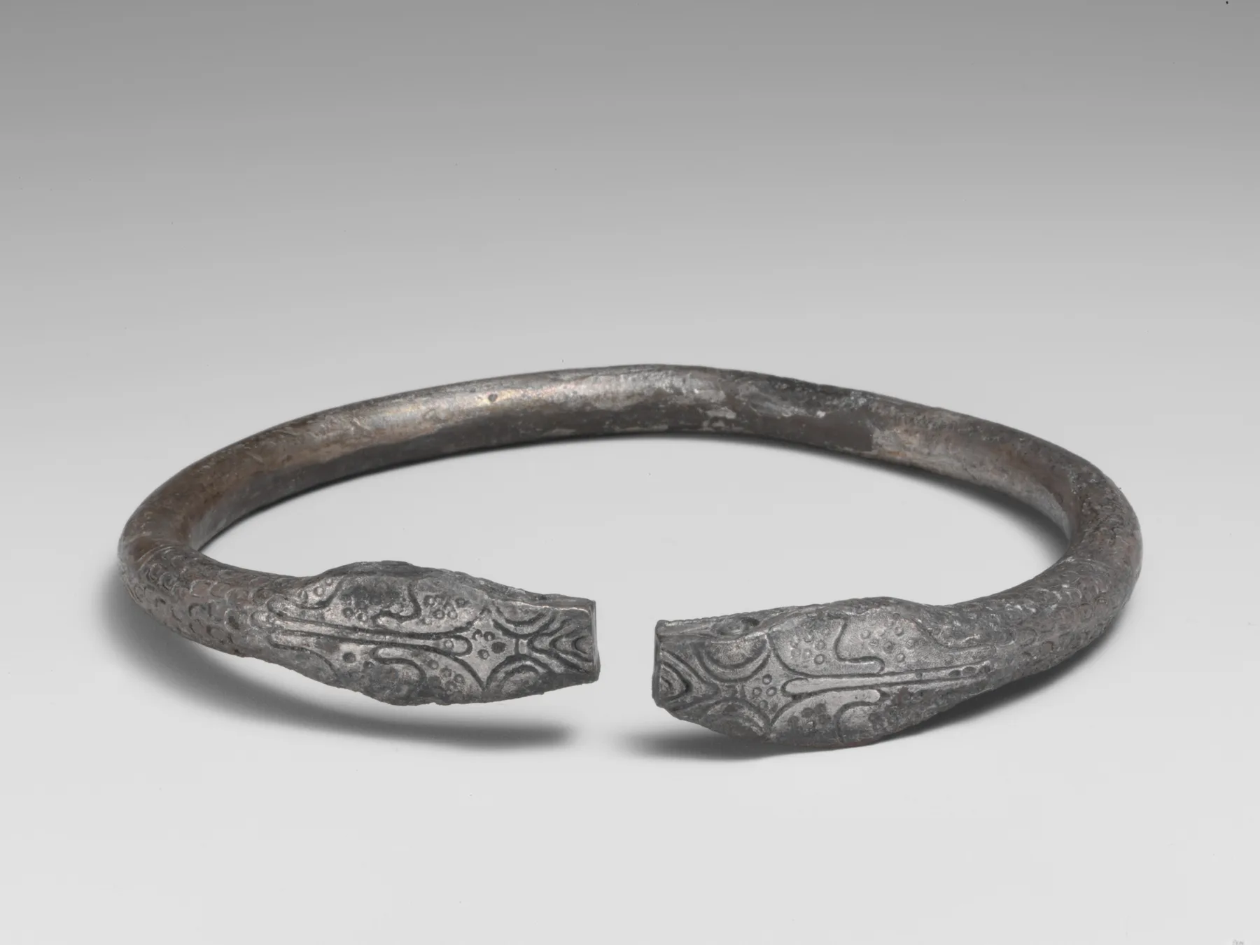 Ancient silver open bracelet ending in two engraved snake heads with scale texture behind each terminal