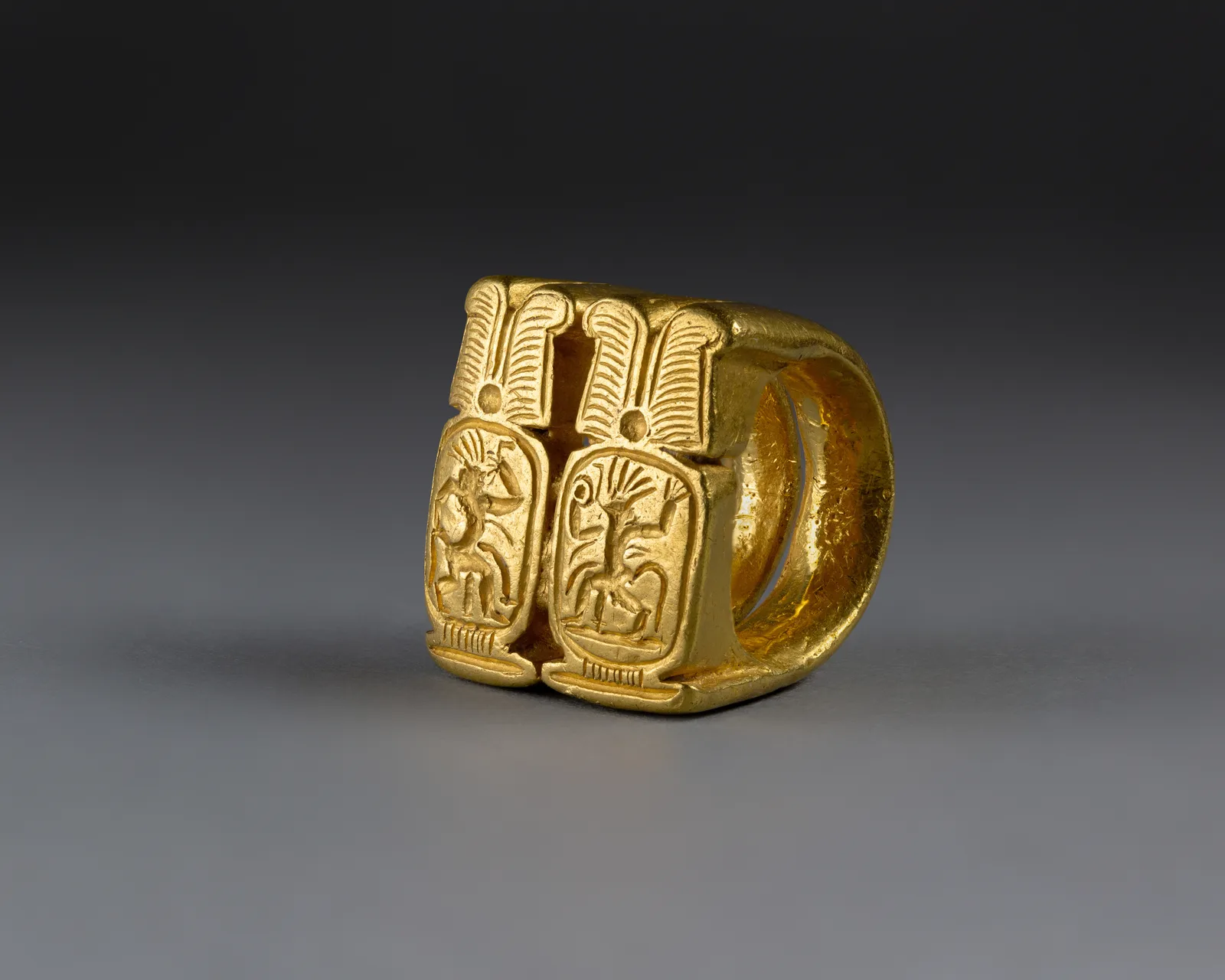 Amarna gold signet ring whose bezel is two cartouches side by side, each with a dancing Bes, ostrich plumes above