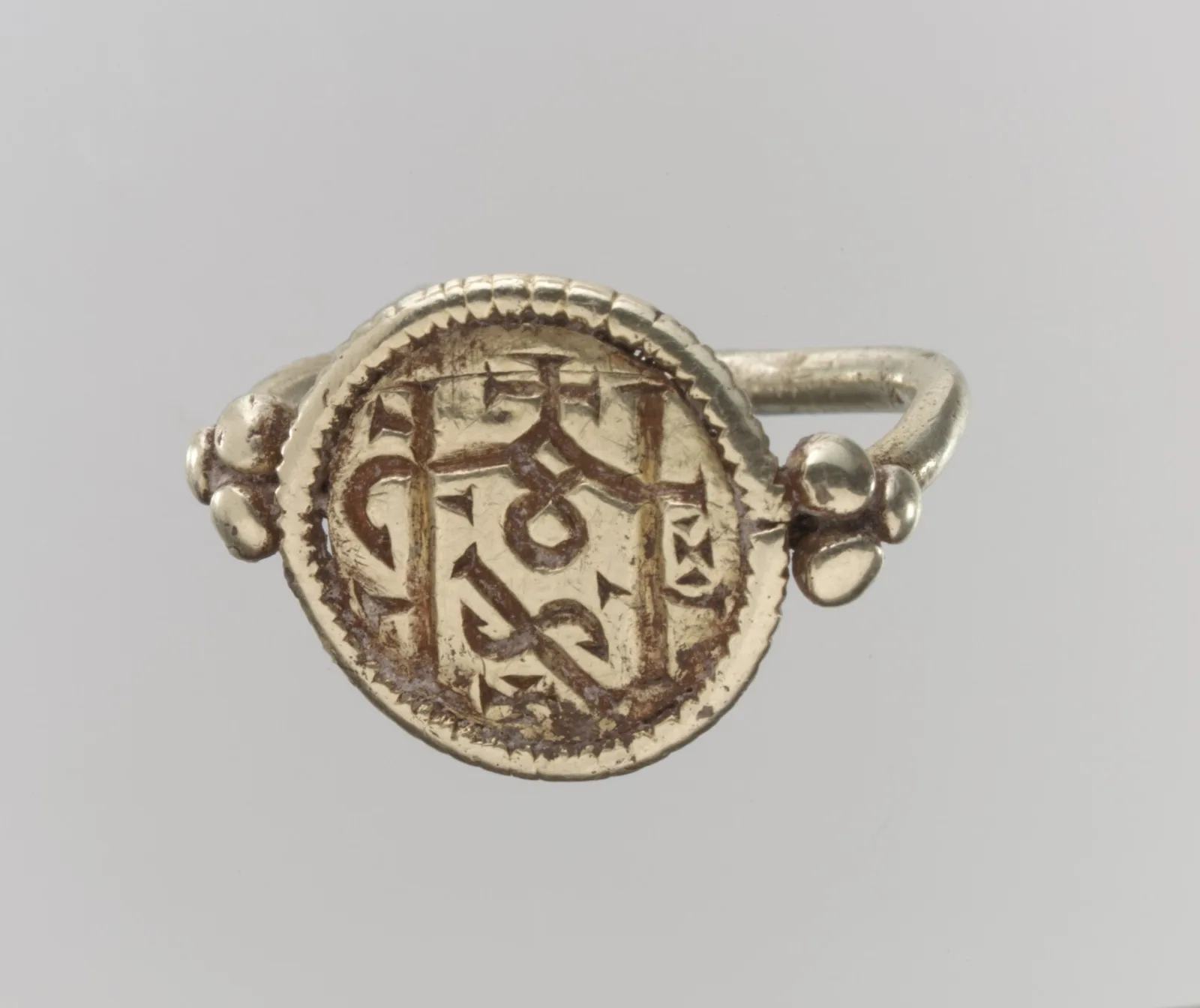 Frankish electrum signet ring with a round flat face cut as a monogram, small knobs at the shoulders