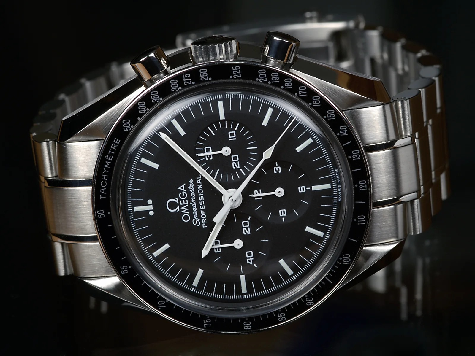 Omega Speedmaster Professional with a dark dial, three registers, and a tachymeter bezel, shown off the wrist