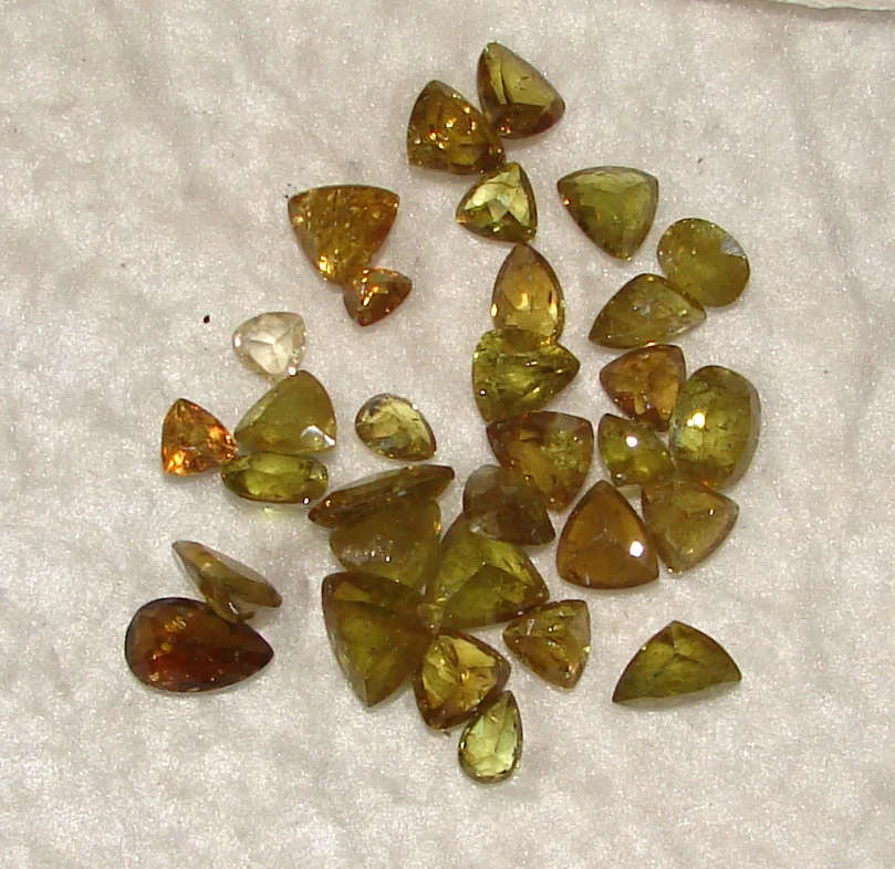 Two faceted sphene gems, one oval and one step-cut, yellow-green on a white ground