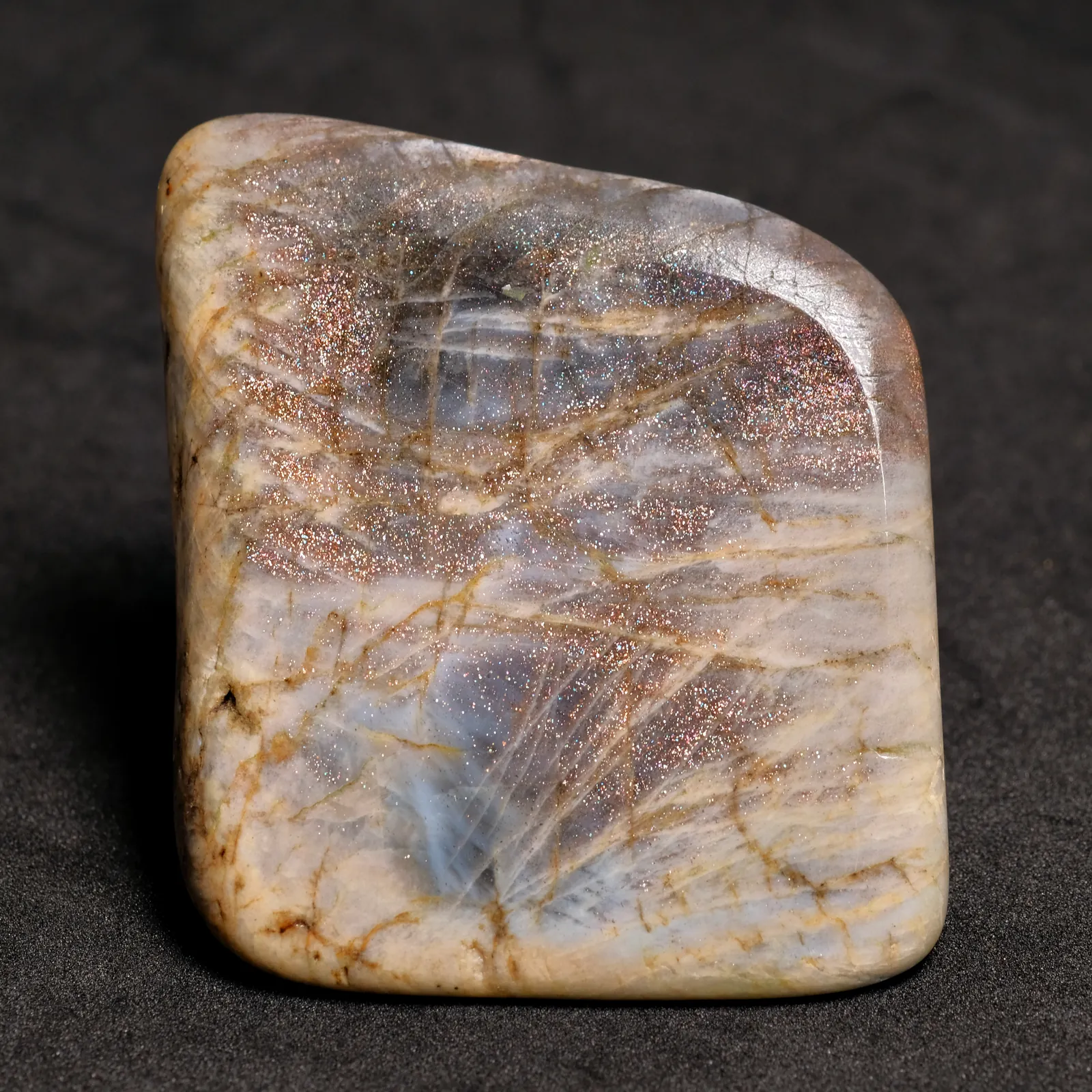 Studio still of polished sunstone cabochons glittering beside pale moonstone on a light ground