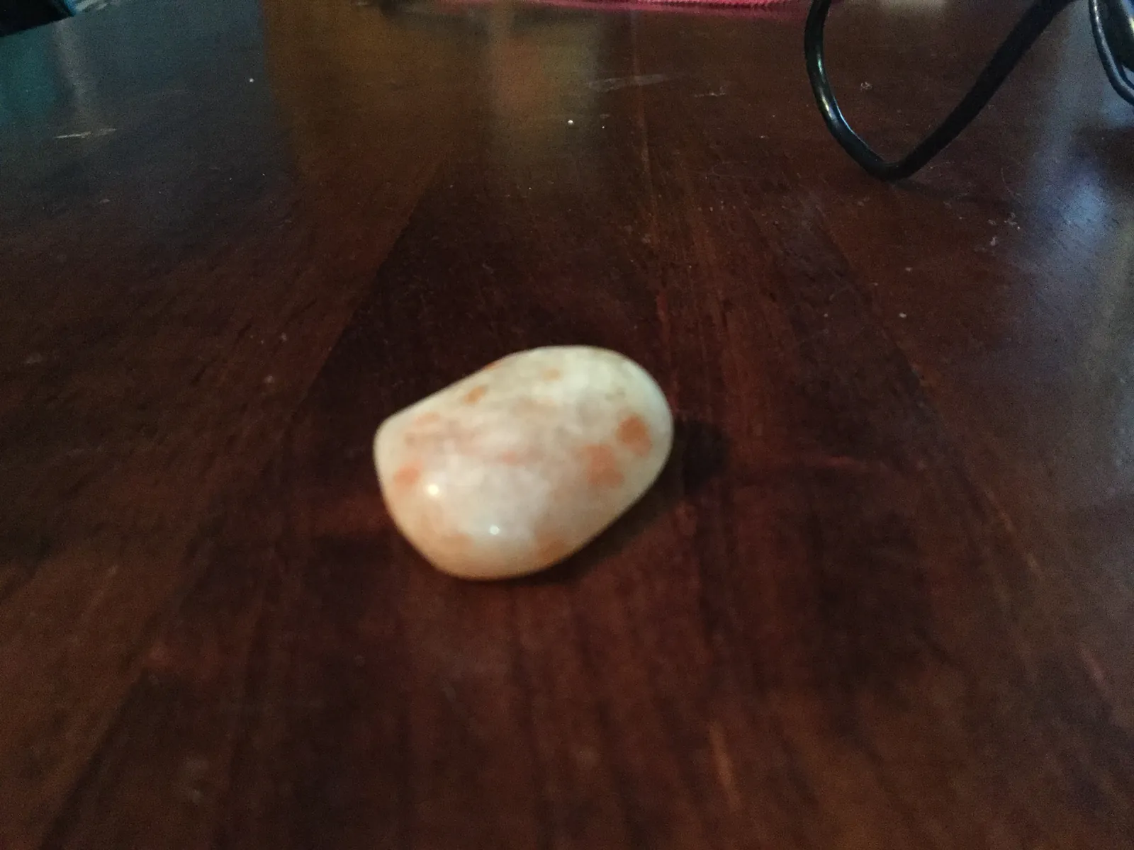 Polished orange sunstone cabochon on a light ground, coppery glitter across the dome