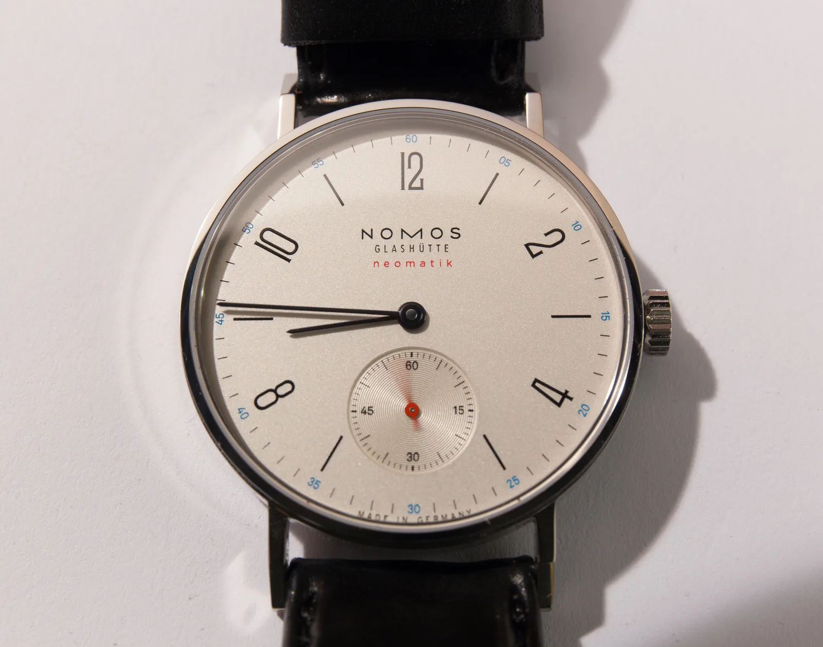 NOMOS Tangente neomatik with a white dial and a slender case, shown off the wrist on a white ground