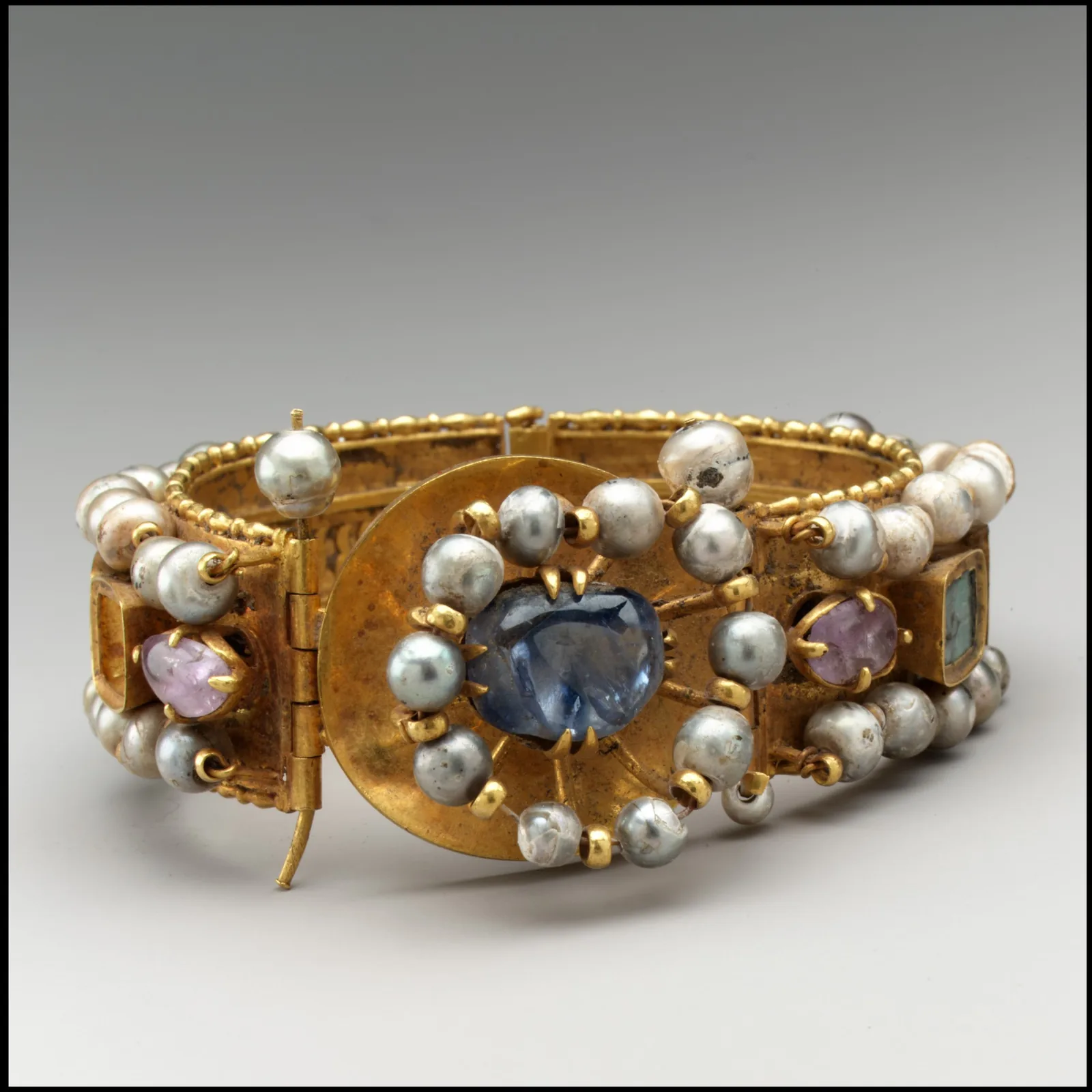 Byzantine gold bracelet with a central violet-blue sapphire in a pearl halo on a gold disk, smaller pale stones and pearls along the band