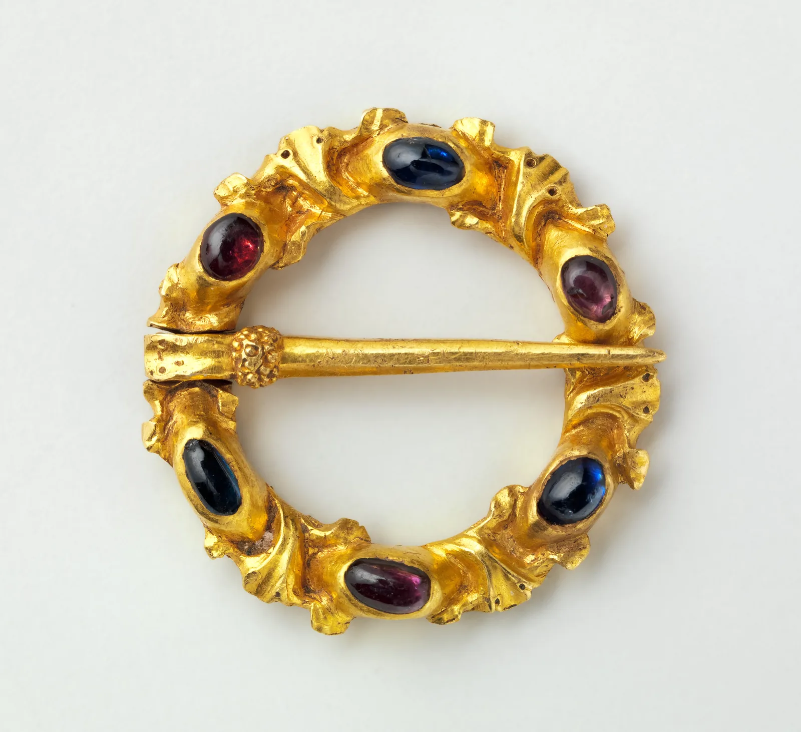 Medieval gold ring brooch set with oval sapphires and garnets around a gold hoop, a pin crossing the open center