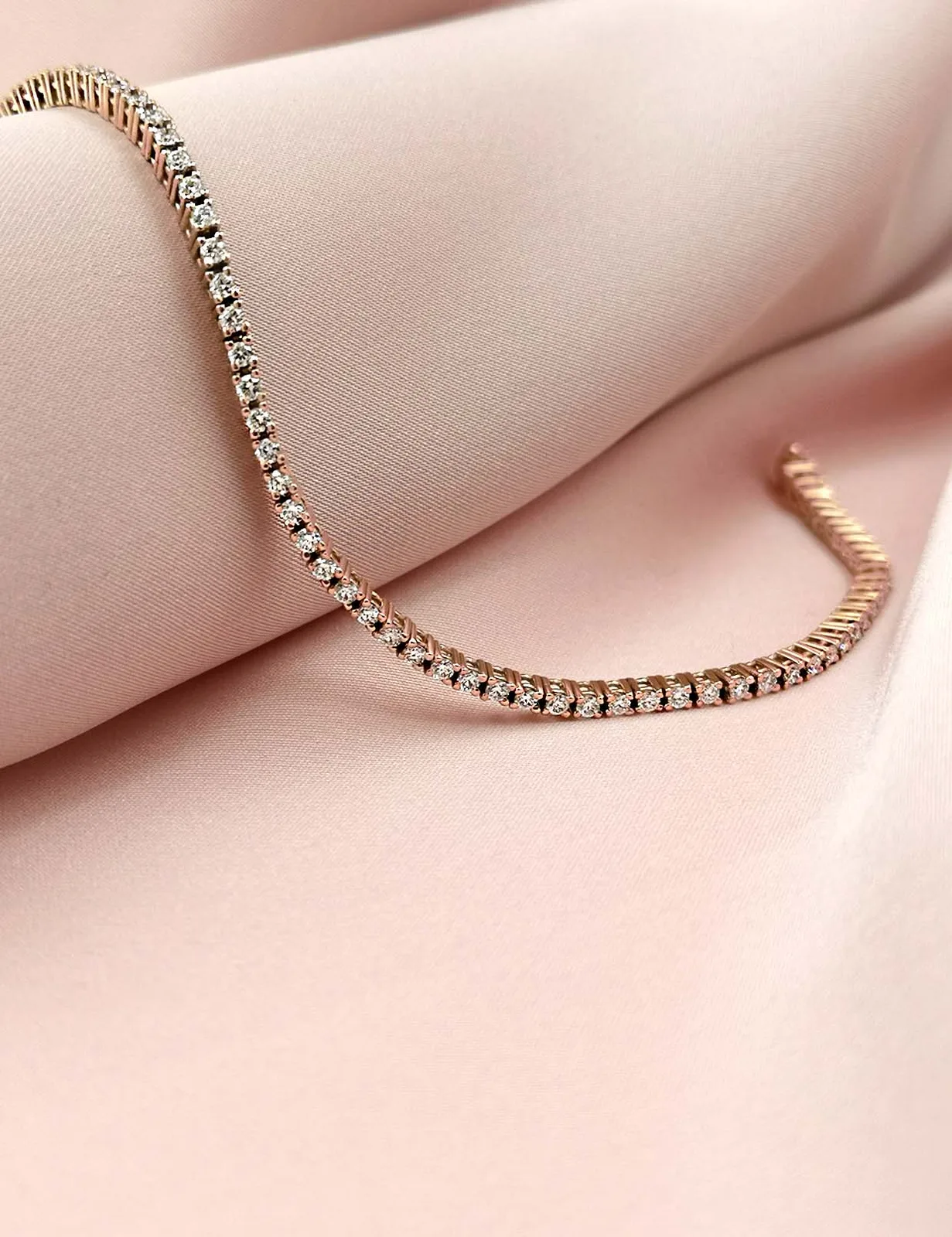 Gold rivière bracelet of matched brilliant-cut diamonds, each stone in its own link, on a pale pink ground