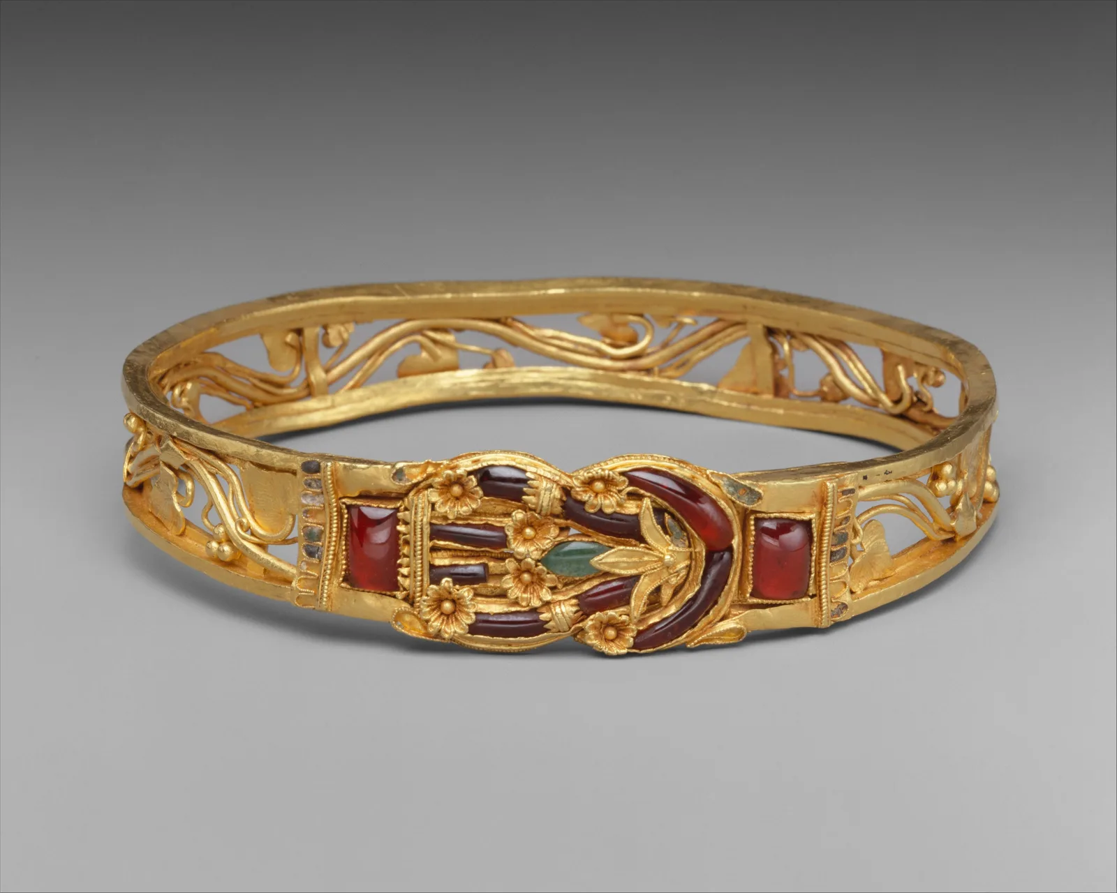 Hellenistic gold armband whose center is a Herakles knot of crossed garnet-inlaid bands, openwork gold around the hoop