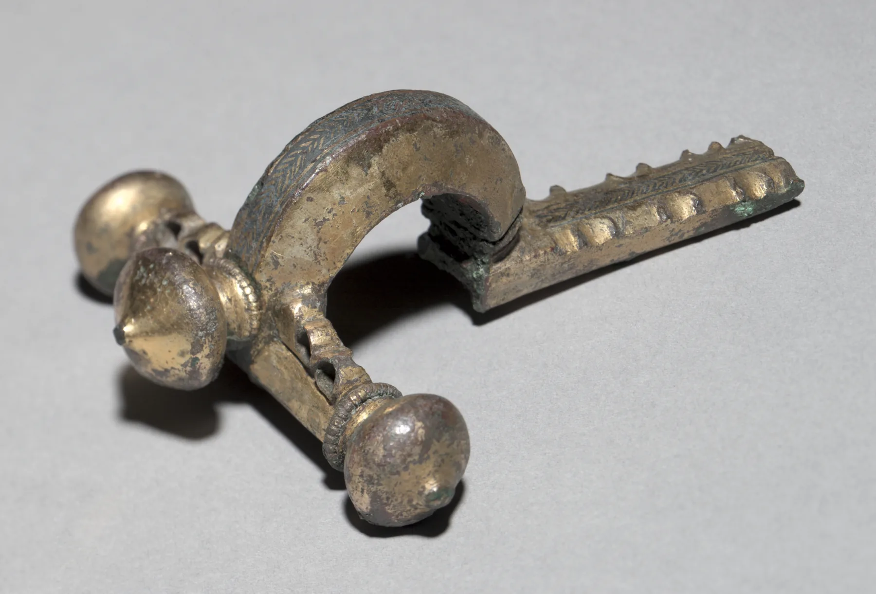 Late Roman gilt-bronze crossbow fibula laid horizontal, a clear T-bar with onion finials and a long foot