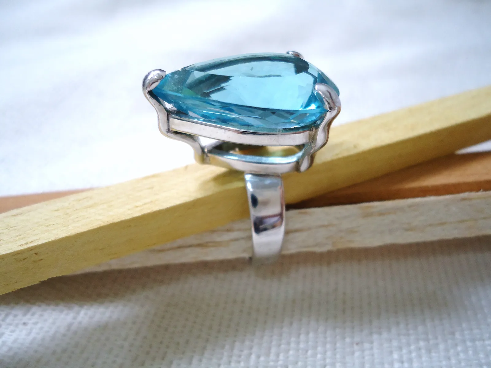 Silver ring with one large round blue topaz and small colorless stones at the shoulders, shown off the hand on a white ground