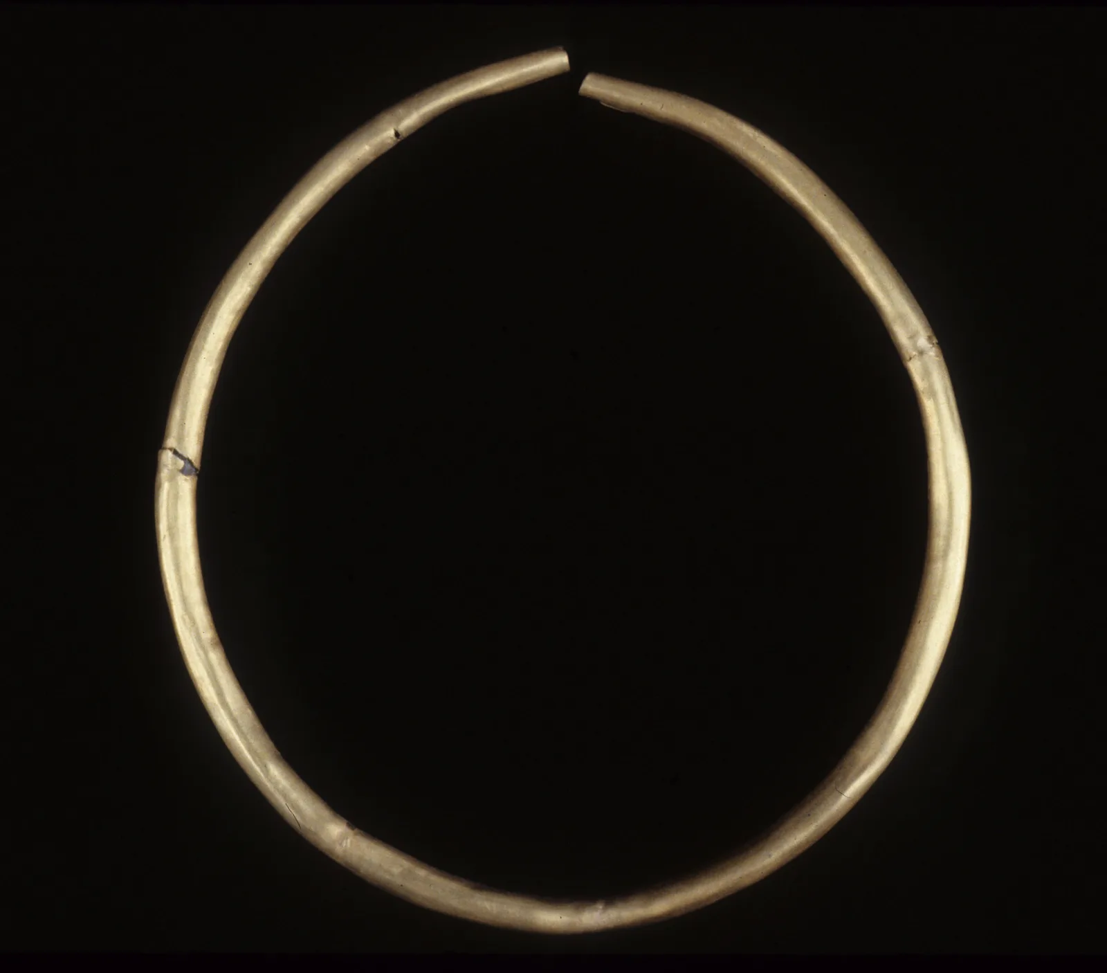 Egyptian gold torque as a single hollow gold tube bent into an open circle, the two blunt ends almost meeting