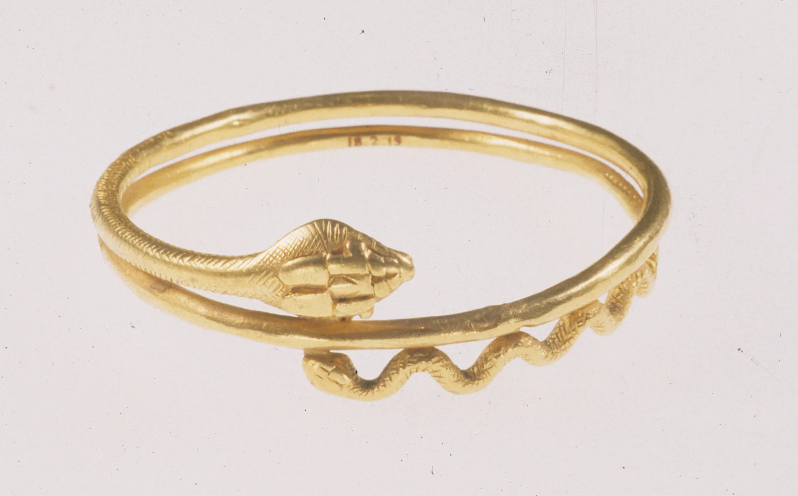 Roman-period gold snake bracelet of two circular turns with a scaled head and a waving tail, museum number painted inside the hoop