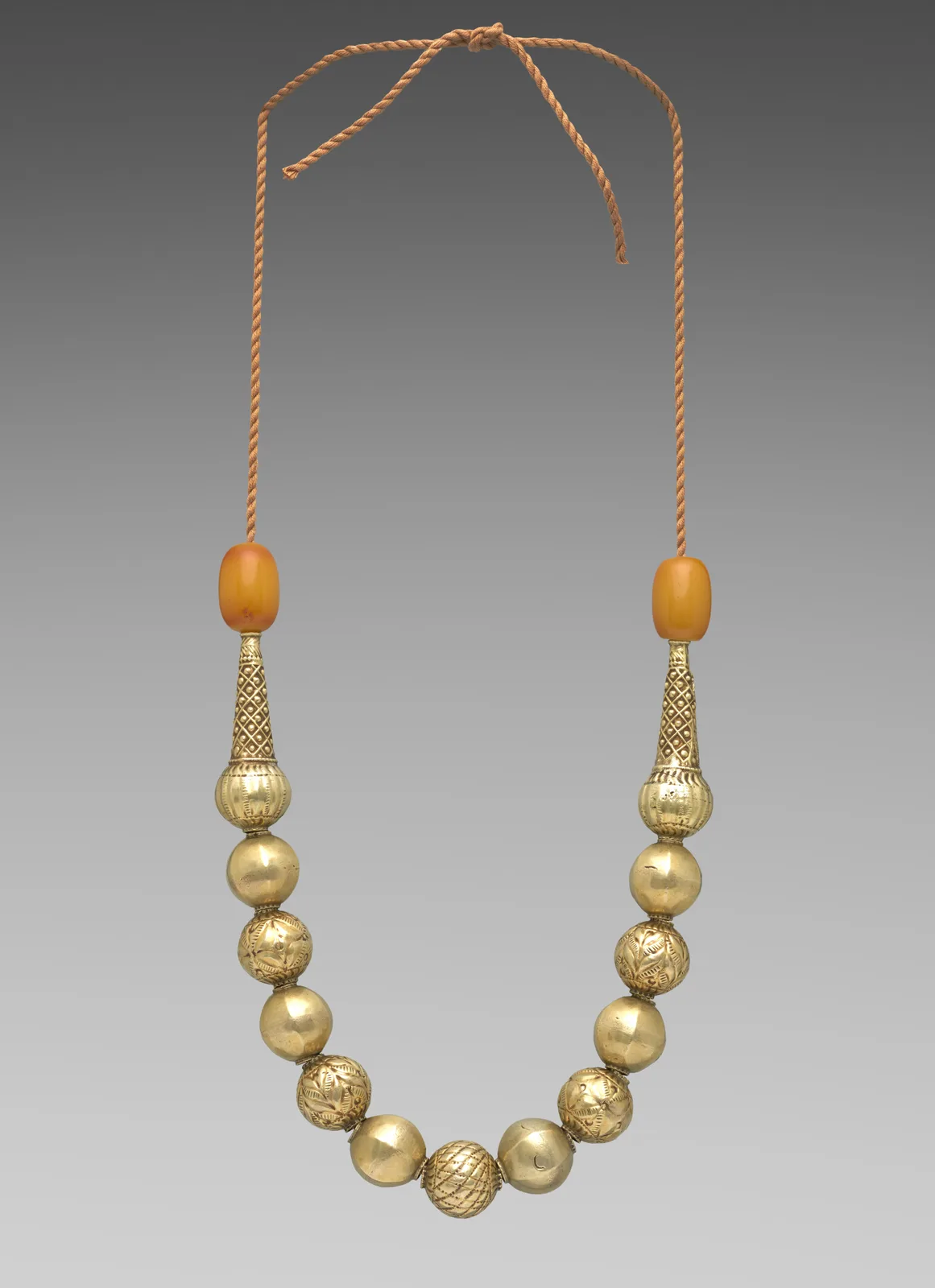Ethiopian gilt-silver bead necklace of round gold-looking spheres with a tapered terminal and a pale resin bead at each end