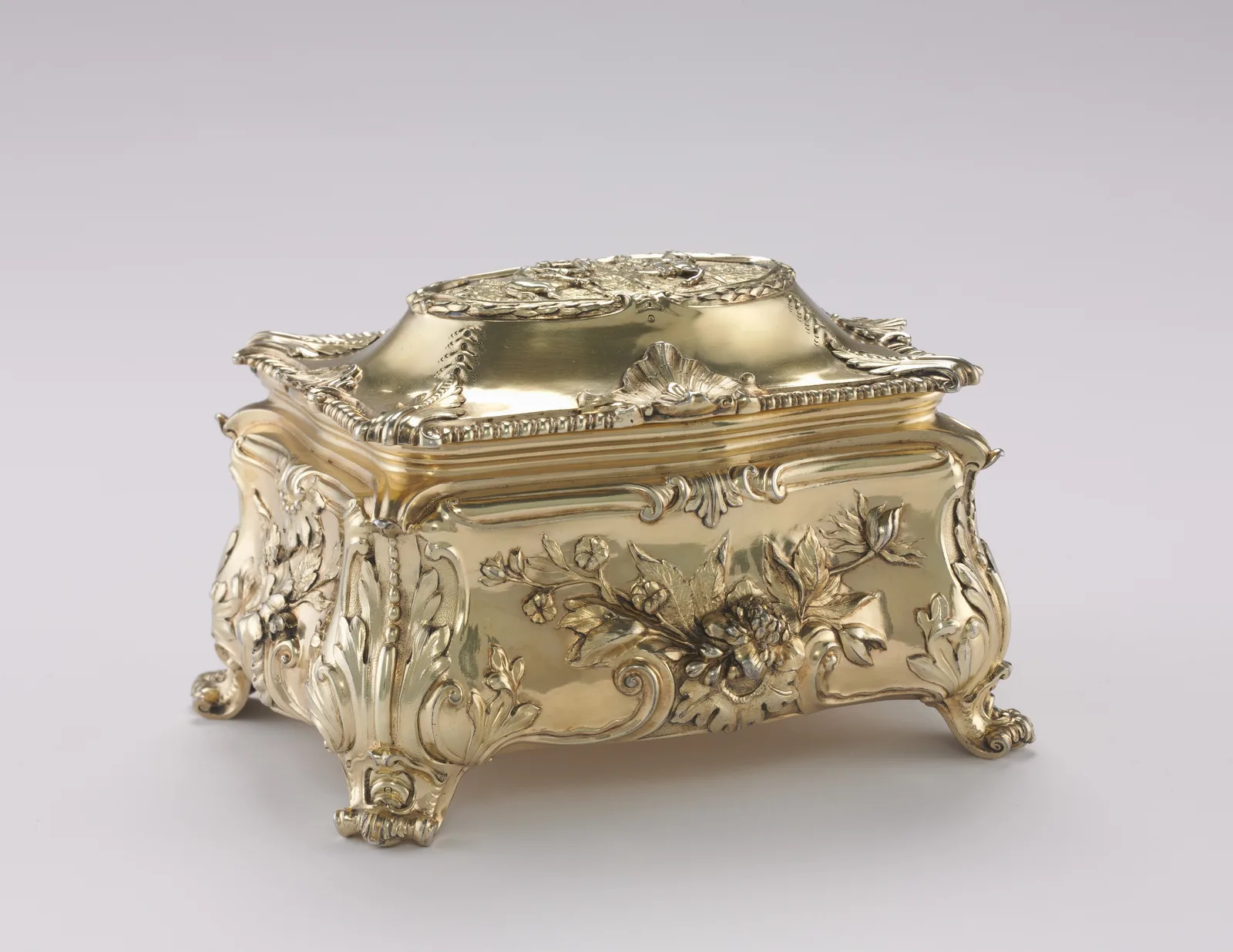 English silver-gilt box of 1771 with chased flowers on the lid and sides, reading as a gold object on four scrolled feet