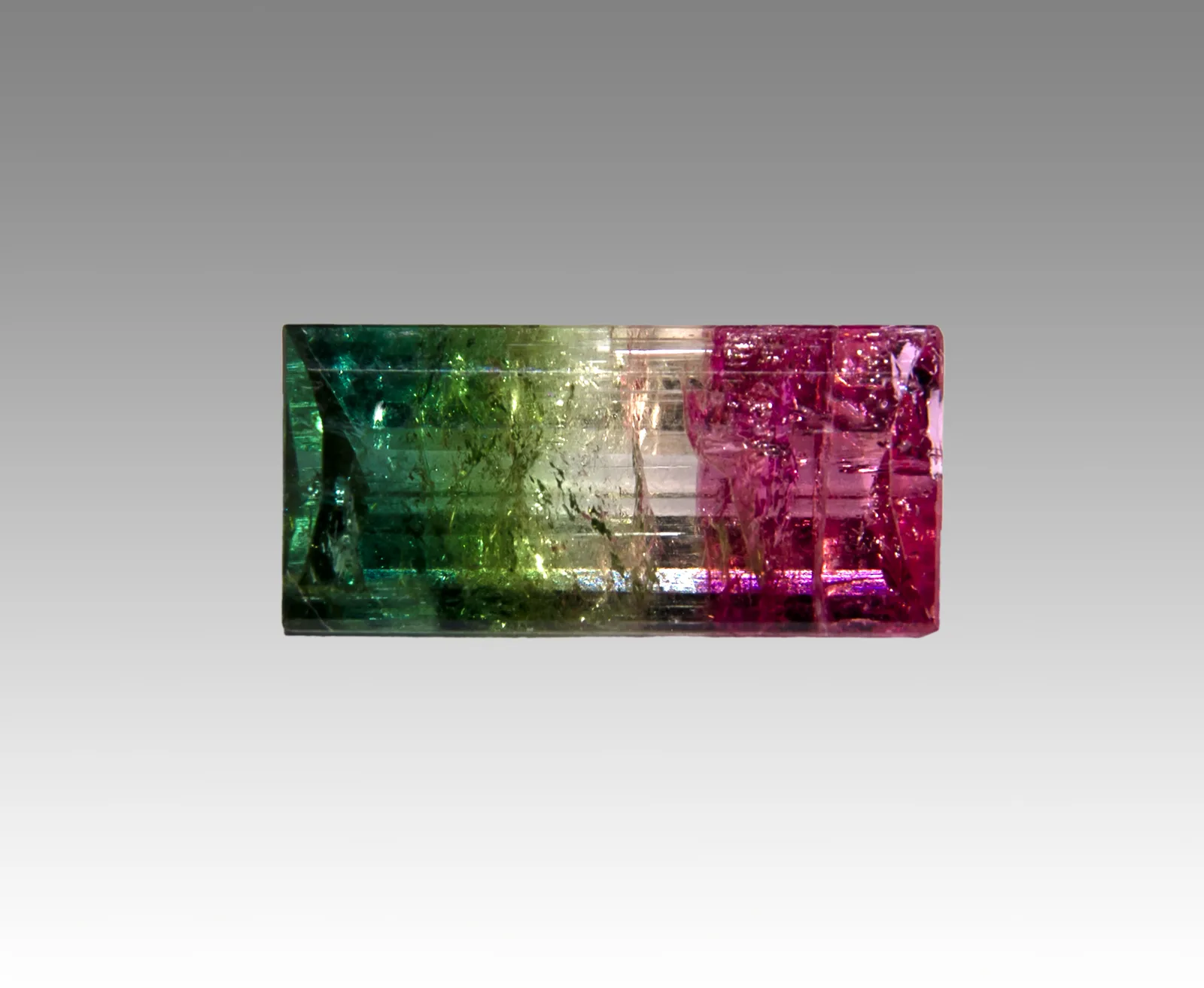 A long faceted watermelon elbaite, pale green warming toward pink along its length, on a white ground