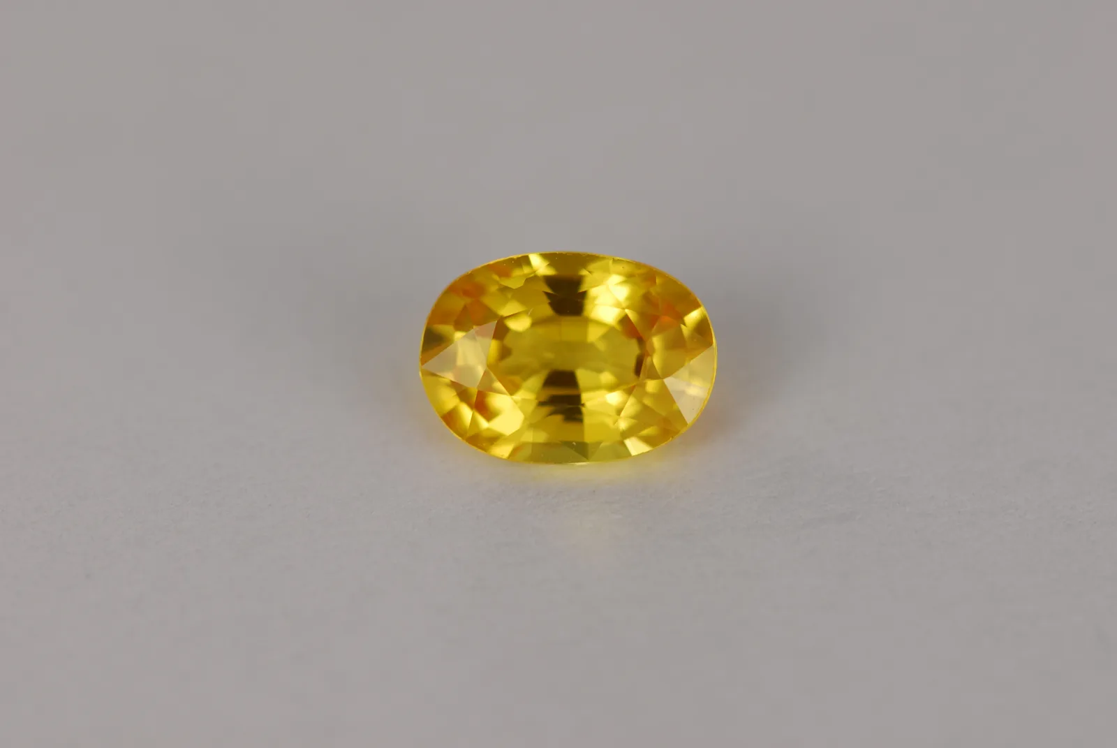 An oval faceted yellow sapphire, golden, on a white ground