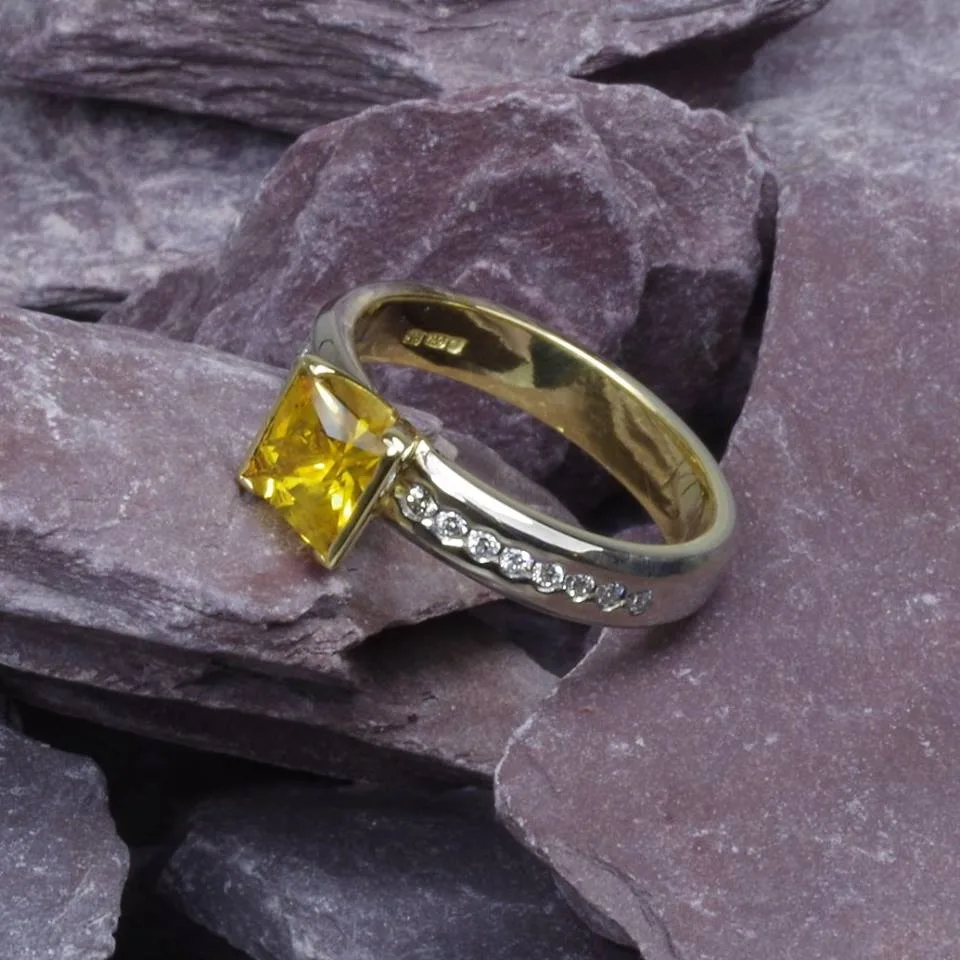 An 18k yellow gold ring with a yellow sapphire flanked by diamonds, on a white ground
